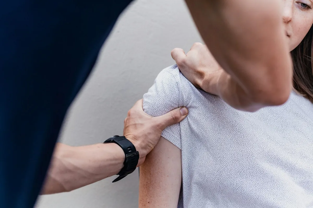 Ostéopathe accompagnant le mouvement de l’épaule d’une patiente assise